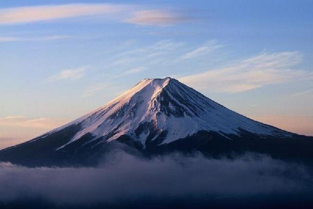 Snow-covered Mount Fuji rising above a band of cloud at dusk
